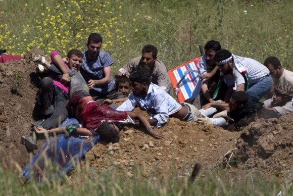 Un grupo de manifestantes palestinos trata de ayudar a un compañero herido por disparos de soldados israelíes cuando trataban de cruzar la frontera desde Siria. Foto: AFP