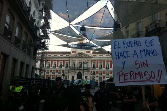 Una pancarta con versos de Silvio Rodríguez en manos de un manifestante, frente a la policía que cerca la Puerta del Sol en Madrid