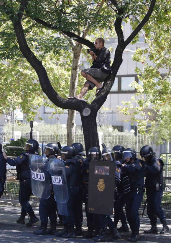 Un fotógrafo encaramado a uno de los árboles de la Castellana y rodeado de agentes antidisturbios. Foto: El País