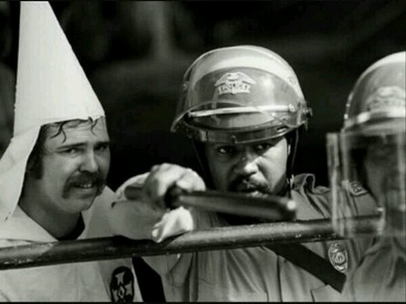 Oficial afroamericano protegiendo a un miembro del Ku Klux Klan de los manifestantes