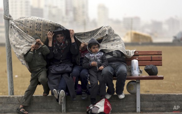 Una familia palestina cubre a sí mismos de la lluvia en el puerto de Gaza, en la ciudad de Gaza, 15 de febrero de 2014. (Foto AP / Hatem Moussa)