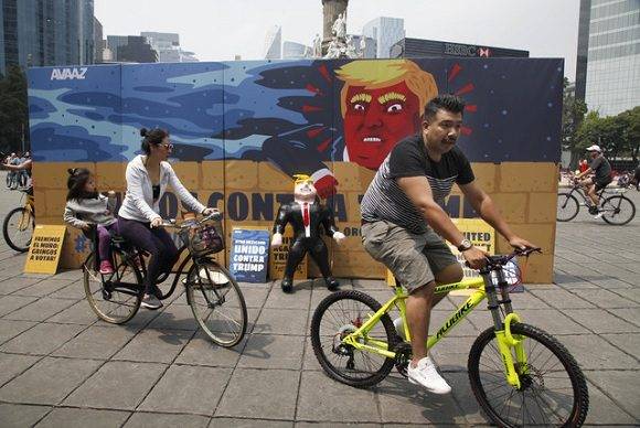 Una pareja pasa en bicicleta junto al mural contra Donald Trump frente al Ángel de la Independencia. Foto: AP.